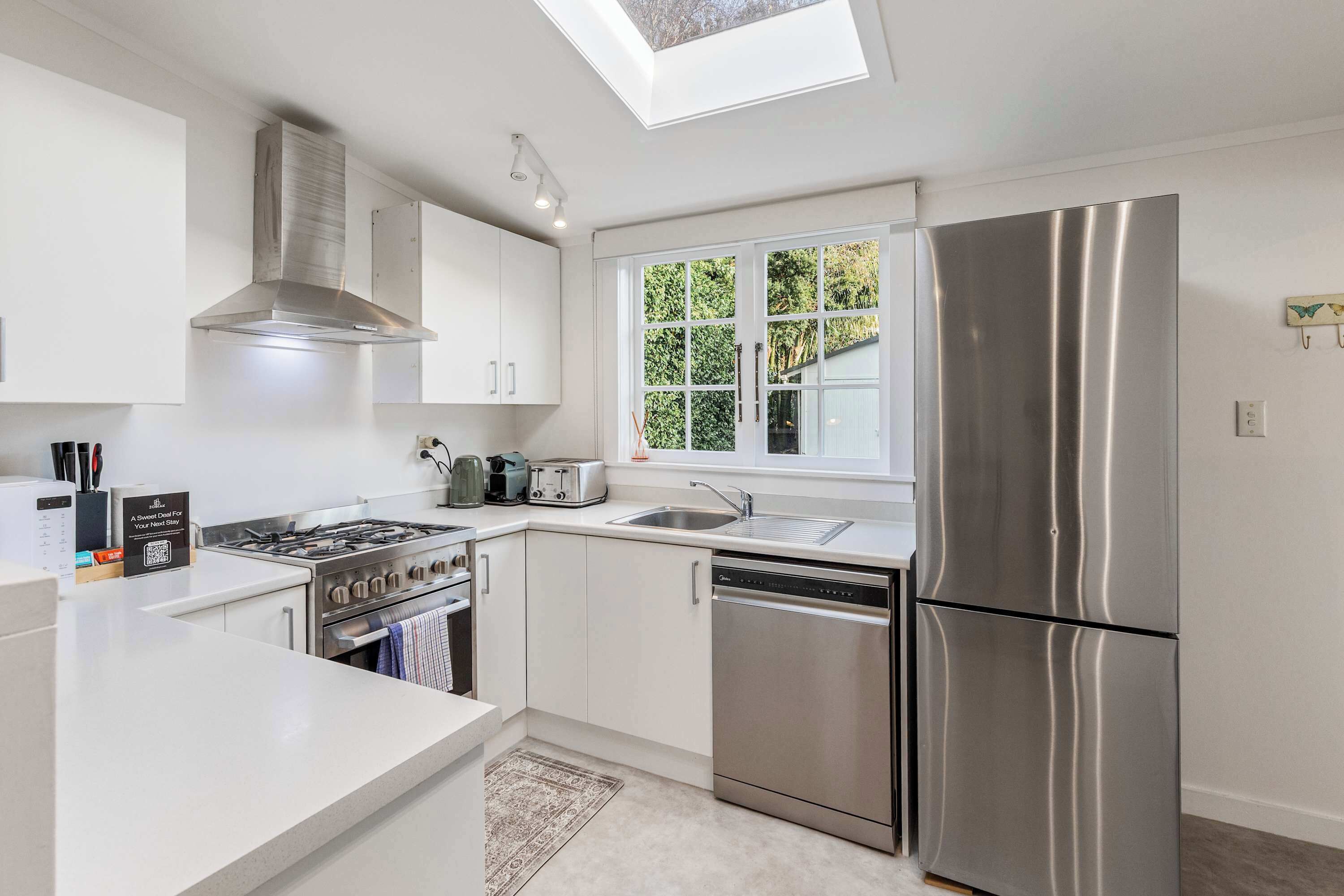 A modern kitchen with a skylight, stainless steel appliances, and a window with a view of greenery.