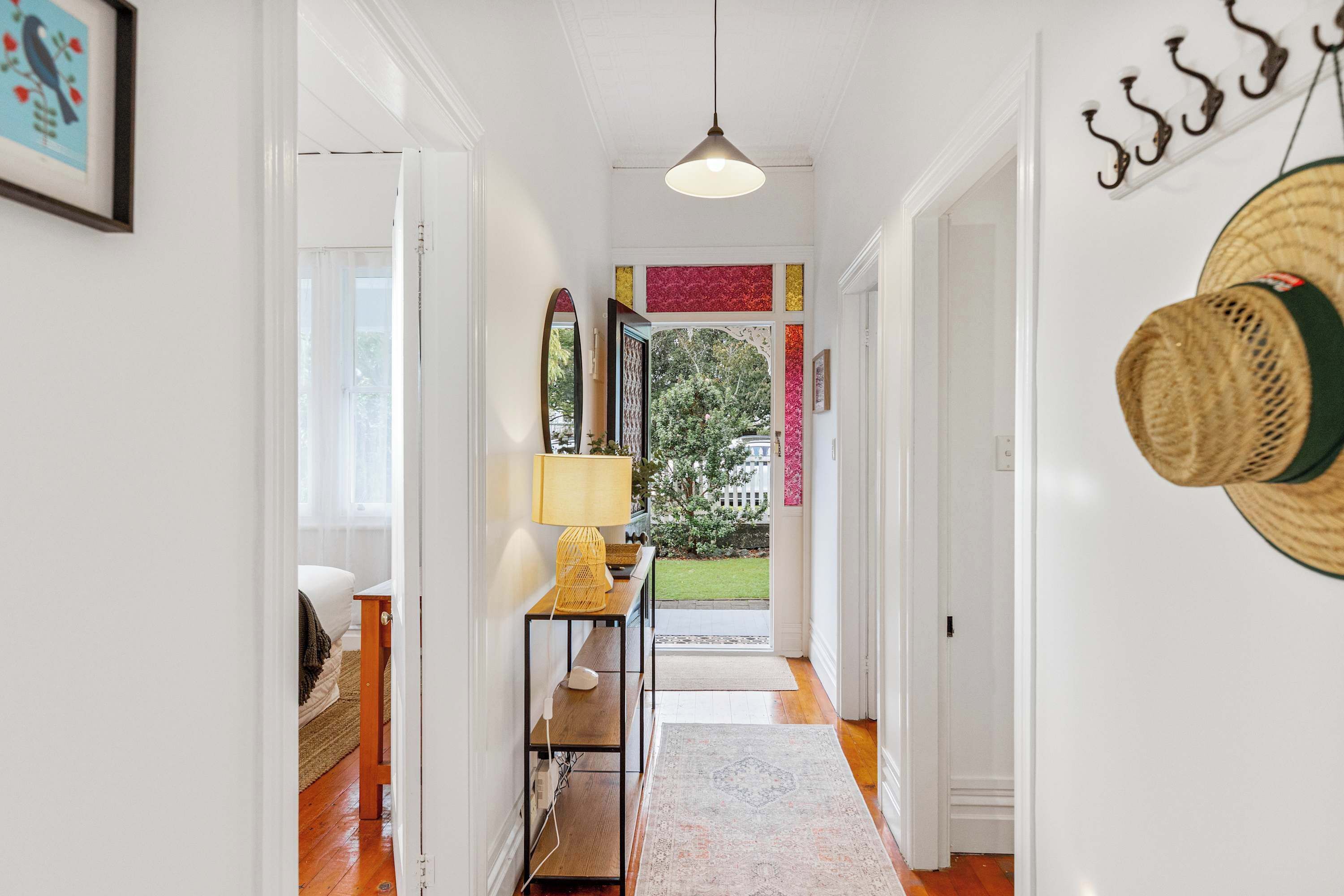 A hallway with a wooden floor, a hanging lamp, a bench, and a view of the outdoors.