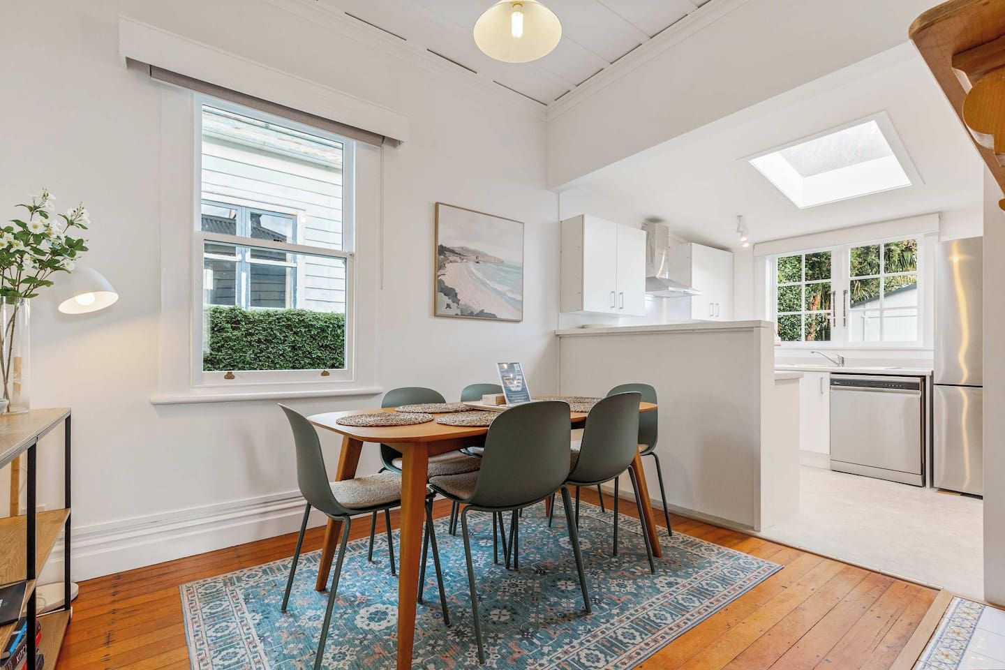 A dining area with a table set for four, surrounded by chairs, a patterned rug, and a window with blinds.