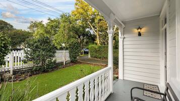 A porch with a white railing, a bench, and a street view with a white fence and trees.