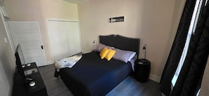 A bedroom with a bed, bedside tables, a desk with a computer, a door, and a wall sign.