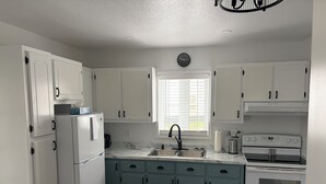 Una cocina con gabinetes blancos, un lavamanos, una estufa y un refrigerador.