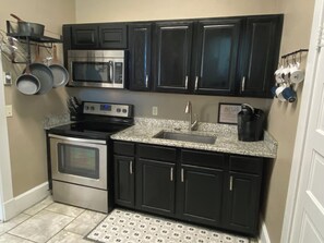 A compact kitchen with dark cabinets, stainless steel appliances, and a granite countertop. - Bison Reserve Suite - Spacious 1-BR Downtown Walkable w/ River & Waterfall Views (Hot Springs)
