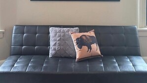 Una habitación con un sofá de cuero oscuro, una obra de arte en la pared que representa un bisonte y una ventana con persianas.