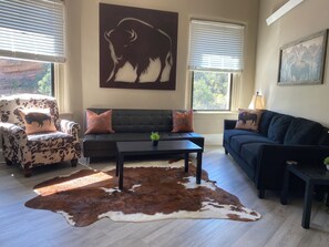 A living room with a sofa, armchair, and a cowhide rug. - Bison Reserve Suite - Spacious 1-BR Downtown Walkable w/ River & Waterfall Views (Hot Springs)