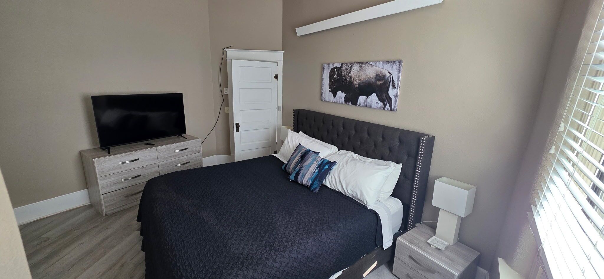 Une chambre à coucher comprenant un lit, une télévision, une commode, une porte et une œuvre d’art accrochée au mur.