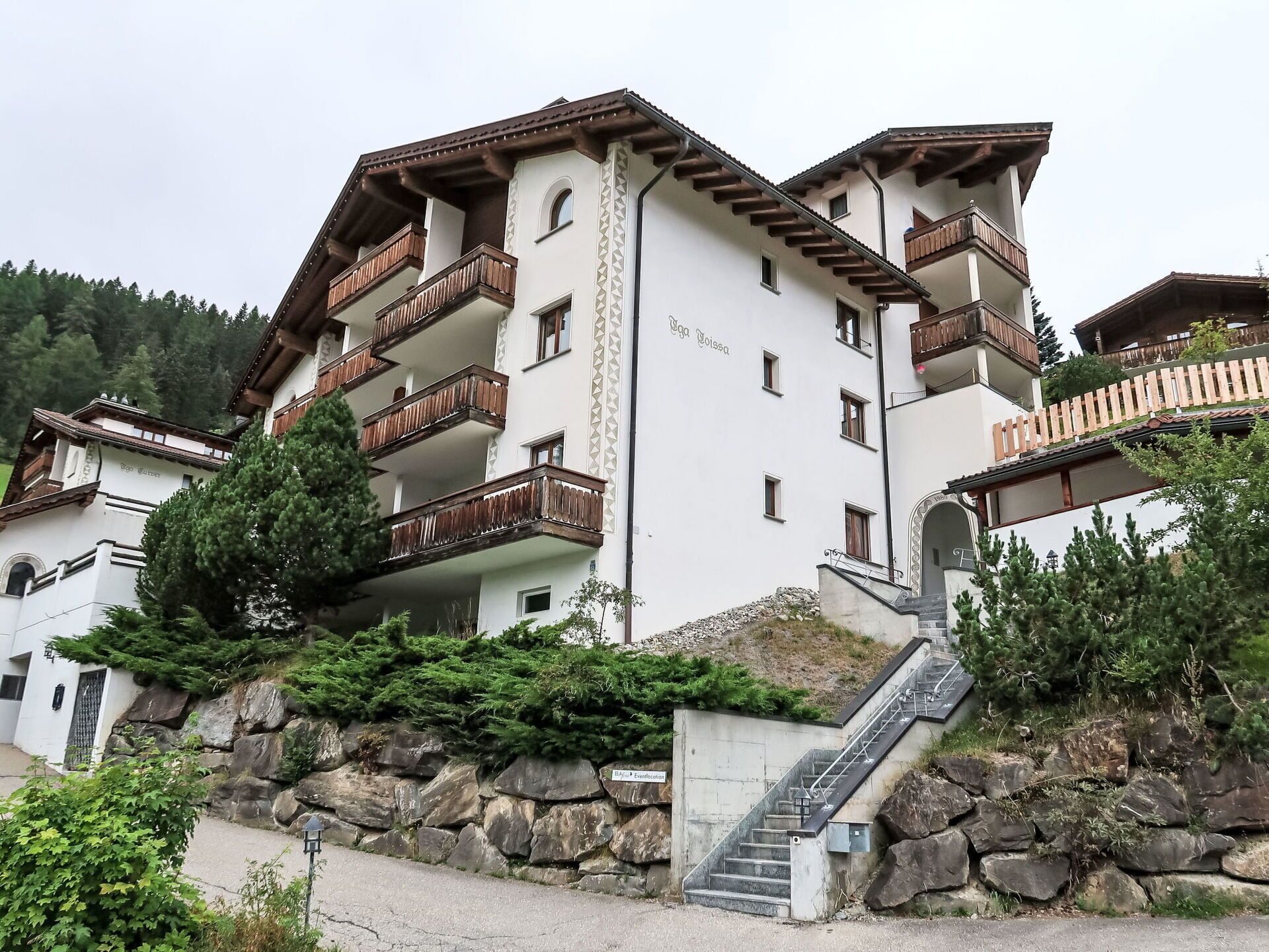A multi-story building with balconies, a stone staircase, and a sign indicating a restaurant.