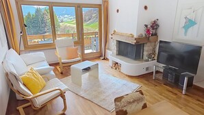 Un saló amb una xemeneia, televisió i un finestra gran amb vista a un paisatge de muntanya.
