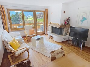 Ein Wohnzimmer mit Kamin, Fernseher und großem Fenster mit Blick auf eine Berglandschaft.