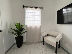 A room with a potted plant, a white chair, a curtain, and a wall-mounted TV. - Cozy 1-bedroom apartment in lovely Osbourn with AC (Osbourn)