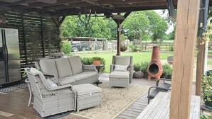 A covered outdoor seating area with wicker furniture, a wooden deck, and a rustic ceiling.