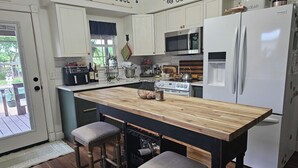 A kitchen with a central island, bar stools, a refrigerator, and a microwave.