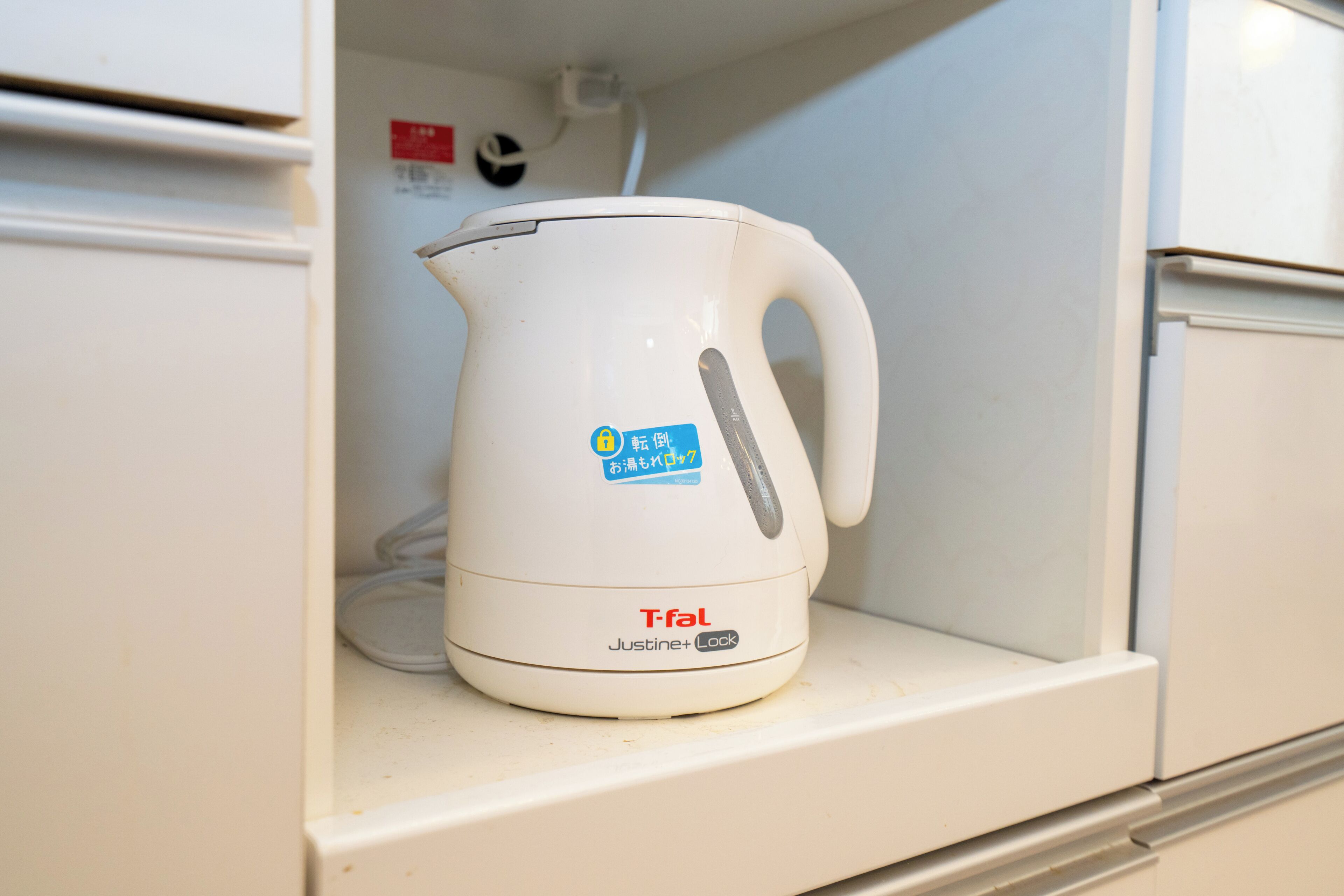 Une bouilloire électrique blanche est posée sur une étagère dans un coin cuisine.