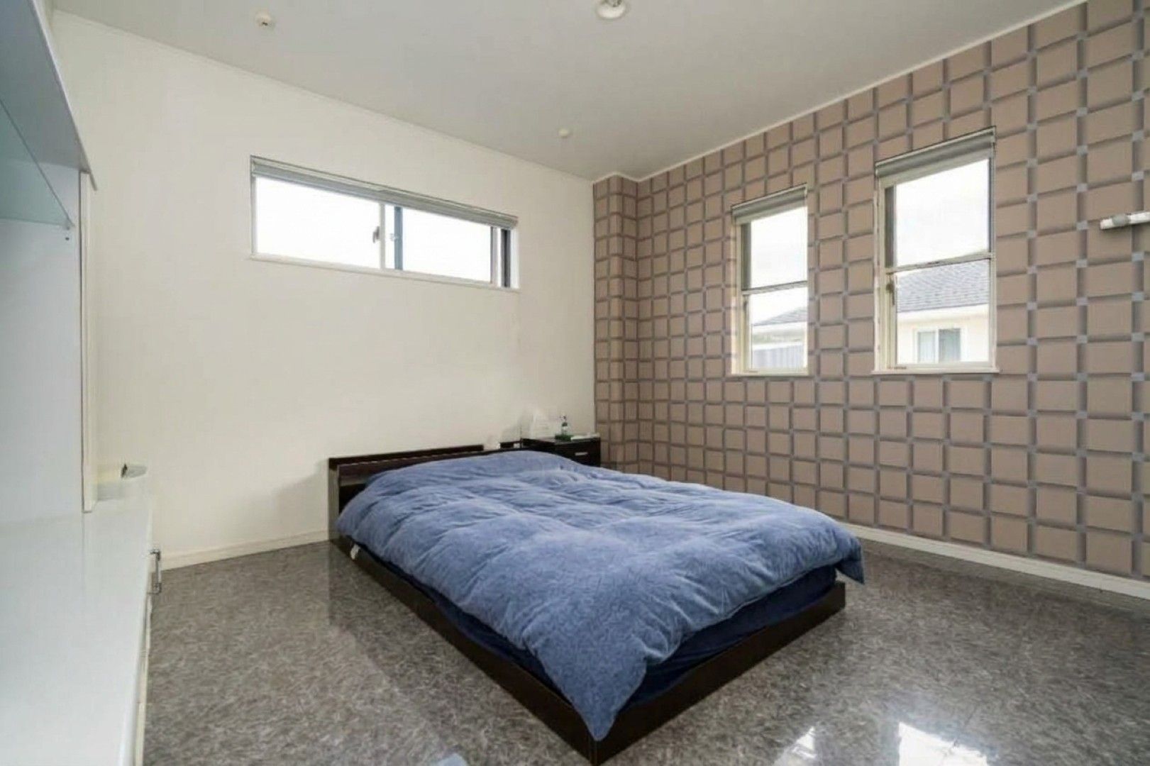 A bedroom with a bed, two windows, a nightstand, and a wall with a geometric pattern.