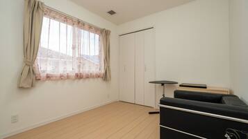 A room with a wooden floor, a black sofa, a small table, a wardrobe, and a window with floral curtains.