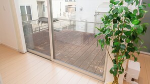 A room with a sliding glass door leading to a balcony with a wooden deck, a potted plant, and a white electrical box.