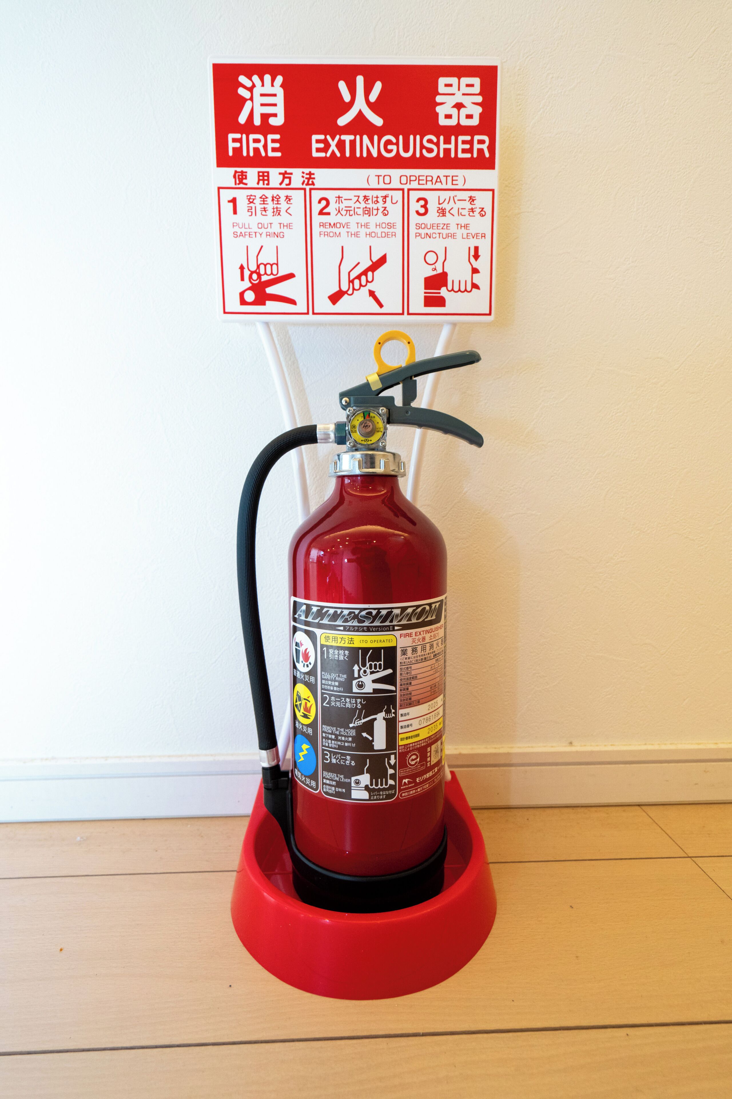 Ein an einer roten Halterung angebrachtes Feuerlöschgerät mit einer Sicherheitshinweisschild über ihm.