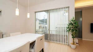 A modern interior with a white table, chairs, a potted plant, and a sliding glass door leading to a balcony.