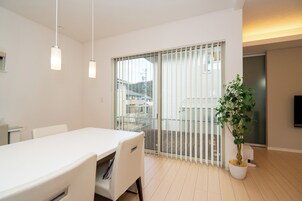 Un interior moderno con una mesa blanca, sillas, una planta en maceta y un cristalero corredizo que da a un balcón.