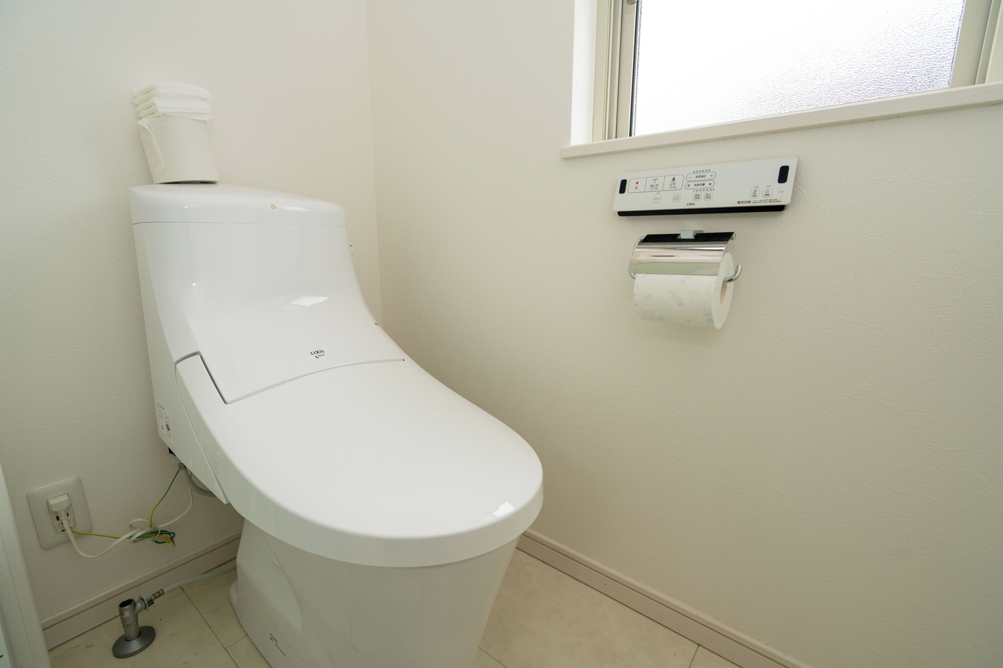 A toilet with a paper towel dispenser and a window above it.