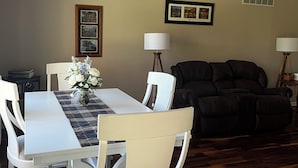 Un coin repas avec une table, des chaises et un vase de fleurs. On y trouve également un canapé en cuir noir et un tableau encadré au mur.