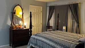 Une chambre à coucher comprenant un lit, une commode, un miroir, une lampe, une chaise et une petite table ronde.