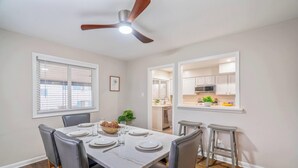 Un coin repas avec une table dressée pour quatre personnes, un ventilateur de plafond et une vue sur la cuisine.