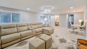 Un salon spacieux avec un grand canapé d’angle beige, un petit pouf et un tapis à motifs.