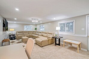 A living room with a sectional sofa, a small table, a bench, and a TV mounted on the wall. - 8 Bells Bungalow - Cozy, Stylish, Prime Location (Annapolis)