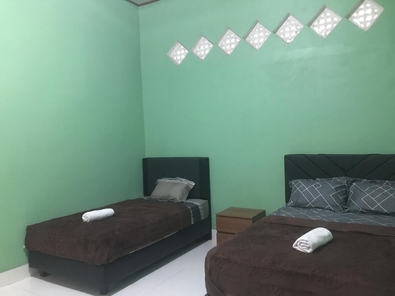 Habitación con dos camas, una mesita de noche de madera y una pared verde con lámparas decorativas.