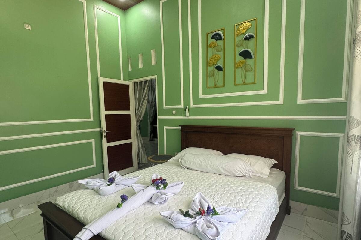 Une chambre d’hôtel avec un lit, une tête de lit en bois, un mur vert agrémenté de moulures décoratives et un miroir.