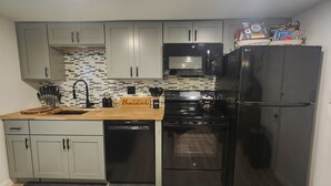 Una cocina con armarios grises, un refrigerador negro, un microondas, un lavavajillas y una encimera de madera.