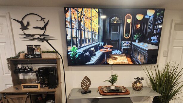 Una sala de estar con una barra de café, un televisor de pantalla plana y un ventanal grande.