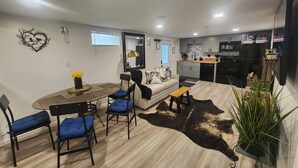 Una cocina moderna con un refrigerador negro, un microondas y una estufa. Hay un comedor con una mesa redonda y sillas azules.