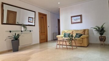Uma sala de estar com um sofá bege, uma mesa de centro, um vaso de plantas, um radiador e um espelho na parede.
