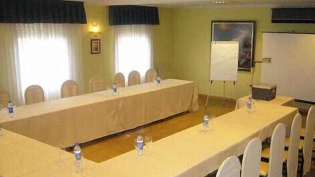 Un salón de conferencias con una larga mesa, sillas, botellas de agua y una pantalla de proyector.