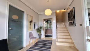 Un interior moderno con una escalera, una mesa de recepción, una planta en maceta y una obra de arte en la pared.