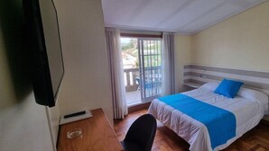 Un dormitorio con cama, una silla, una ventana con cortinas y vistas al exterior.