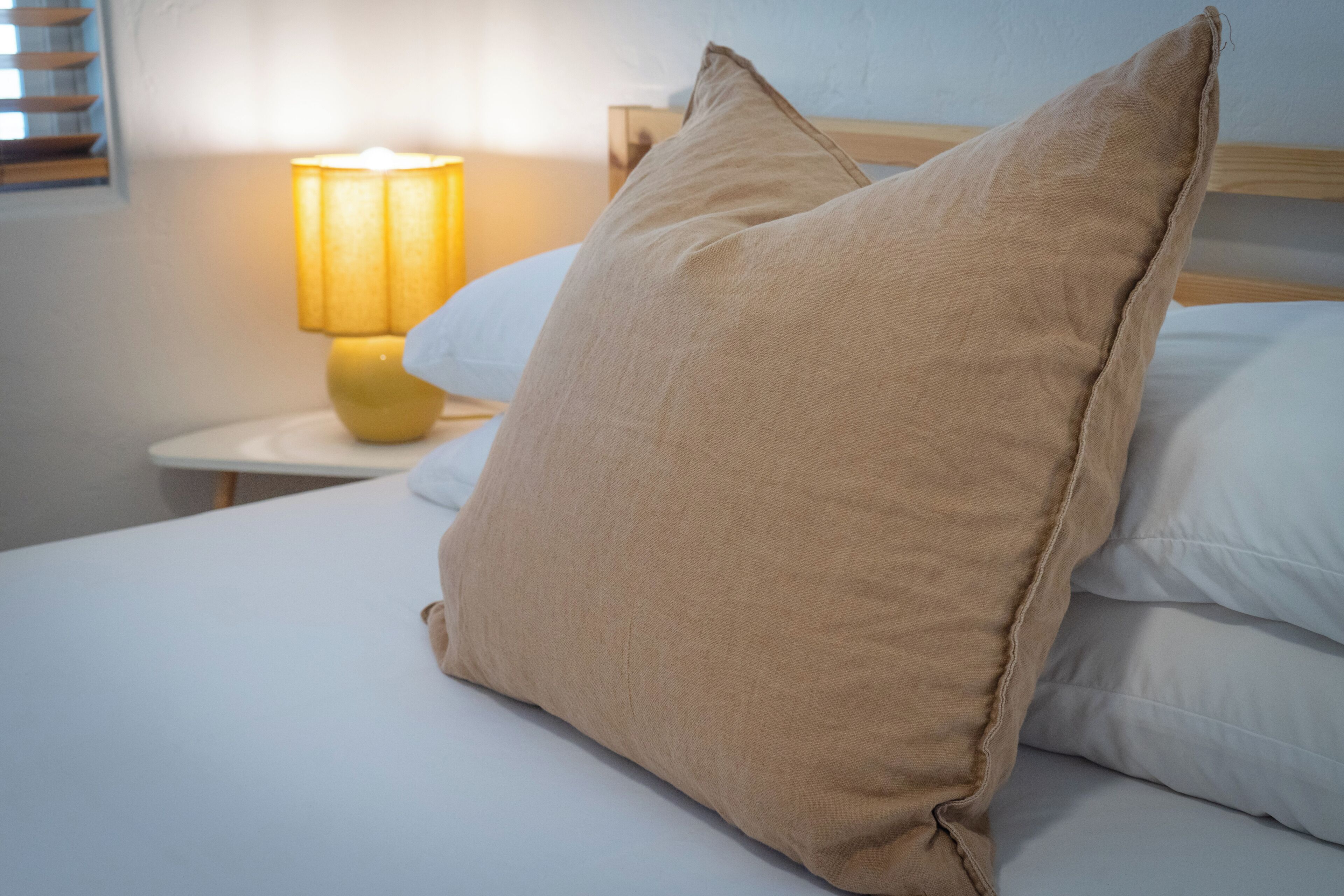 Un lit avec des oreillers de couleur beige, une lampe de chevet et une tête de lit en bois.