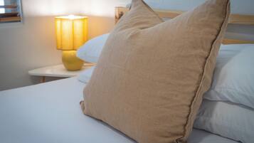 Un lit avec des oreillers de couleur beige, une lampe de chevet et une tête de lit en bois.