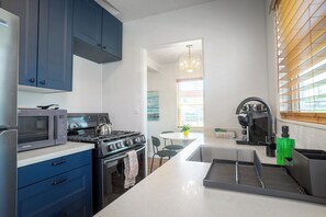A modern kitchen with a microwave, stove, and sink. There is a dining area with a table and chairs. - Charming 1BR bungalow in sunny Ocean Beach with yard (San Diego)
