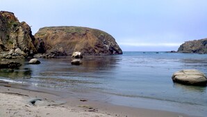 A coastal landscape with rocky cliffs, calm water, and a sandy beach. - Panoramic ocean view 4-bedroom house in charming Gualala perfect for relaxing . (Gualala)