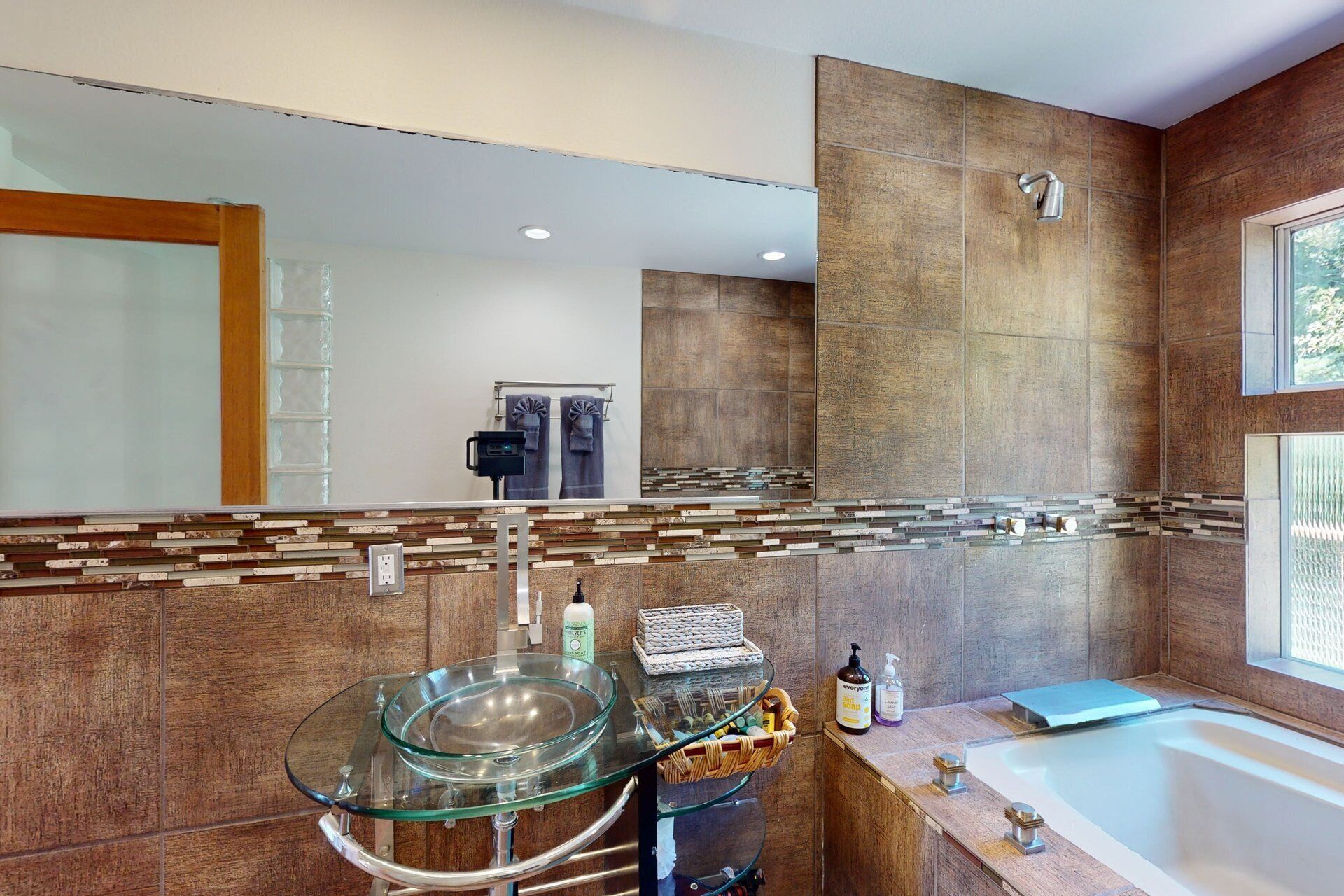 A modern bathroom with a glass sink, a bathtub, and a large mirror.