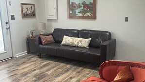 A living room with a dark leather couch, a red armchair, a wooden coffee table, and two framed pictures on the wall.