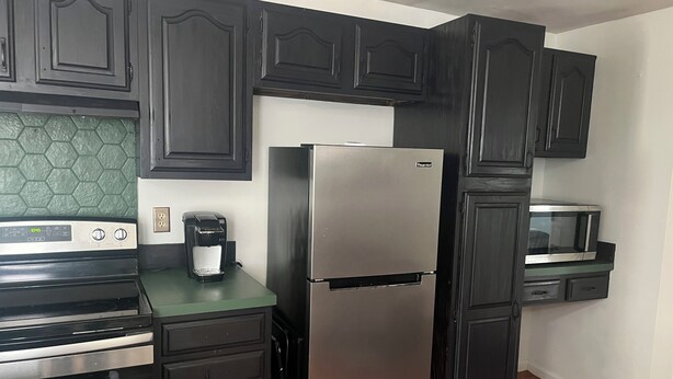 A kitchen with dark cabinets, a stainless steel refrigerator, a microwave, and a coffee maker.