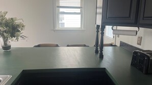 A kitchen with a green countertop, a window with blinds, and a potted plant.