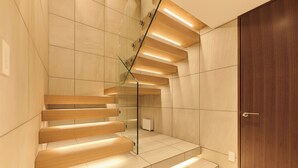 A modern staircase with wooden steps and glass railings, leading to a wooden door.