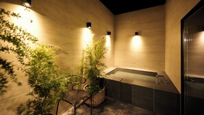 A modern bathroom with a bathtub, potted plants, and wall-mounted lights.