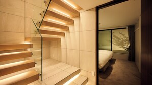 A modern hotel room with a glass staircase, a bed, and a large window.