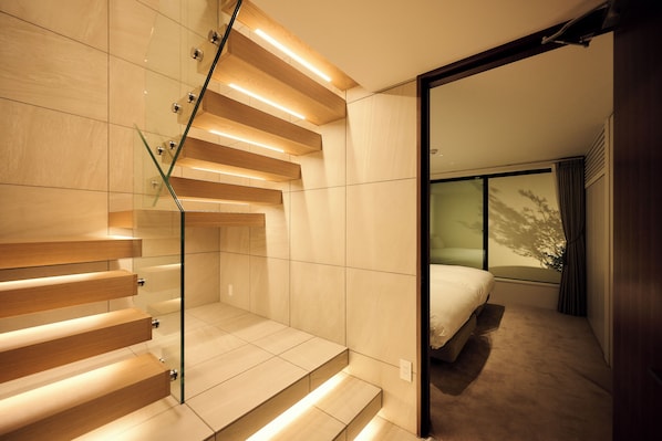 A modern hotel room with a glass staircase, a bed, and a large window.